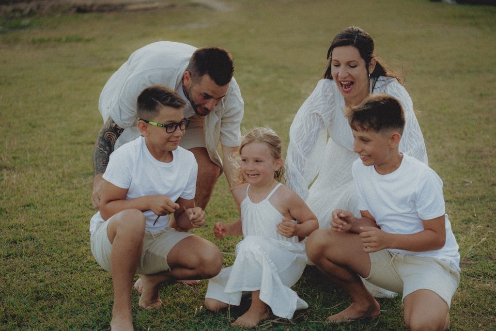 Parents et leurs trois enfants accroupis et riant ensemble sur l'herbe en Guadeloupe, photographe famille CW Photographe